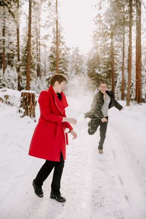 People playing in fresh snow among tall pine trees during winter.