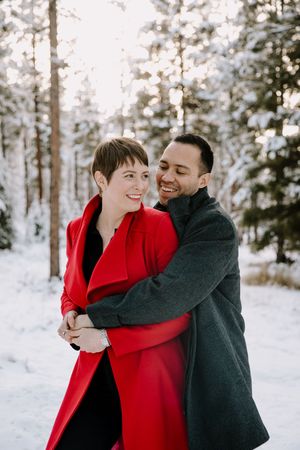 Winter portrait session in a snowy forest with one person wearing a bright red coat.