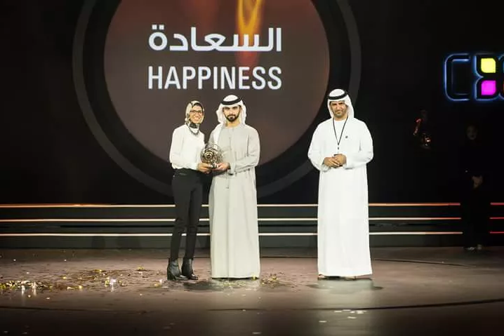 Award ceremony with 'Happiness' text displayed in Arabic and English on stage.