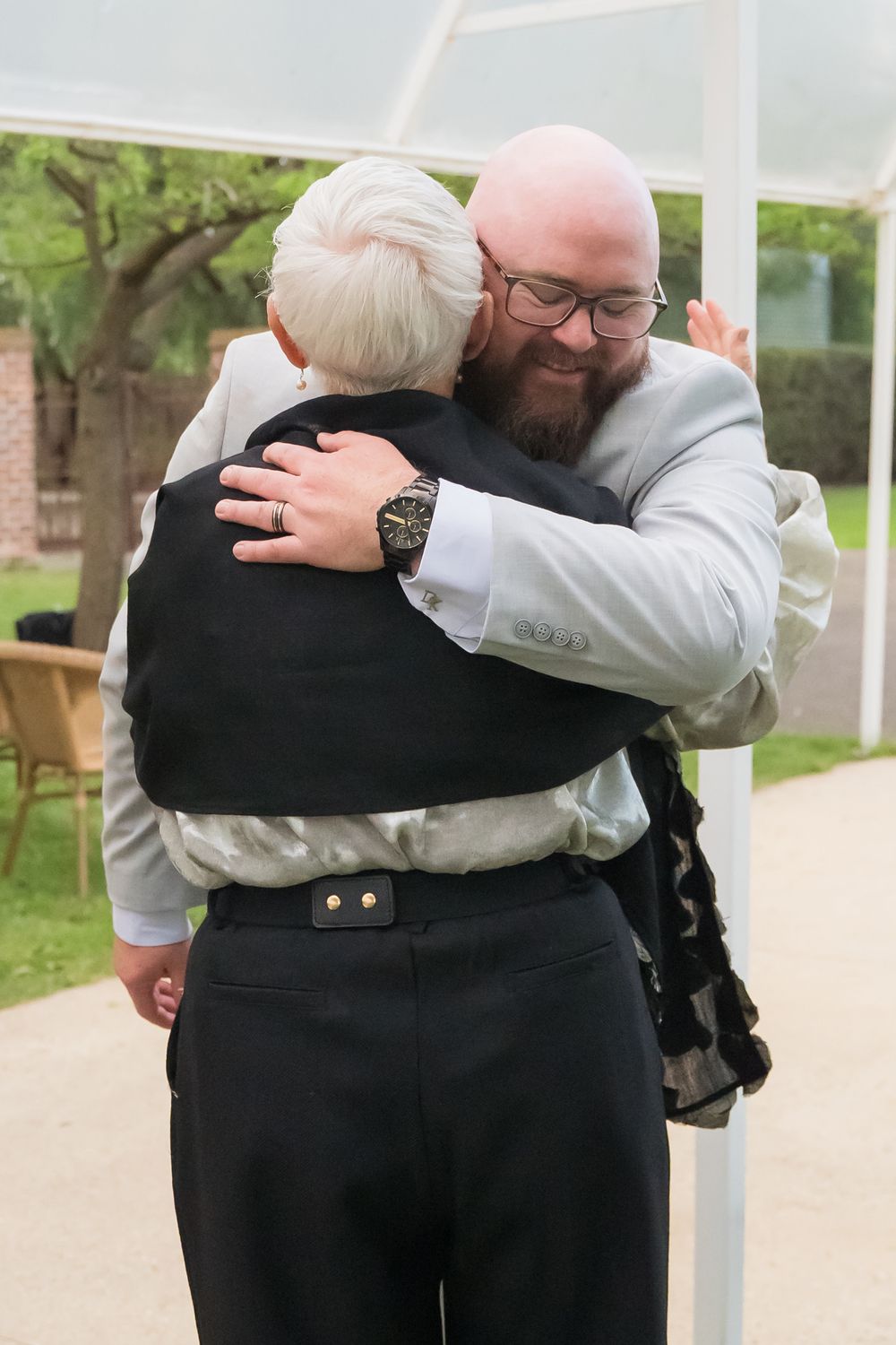 Two men embrace in an emotional moment during a wedding celebration outdoors.