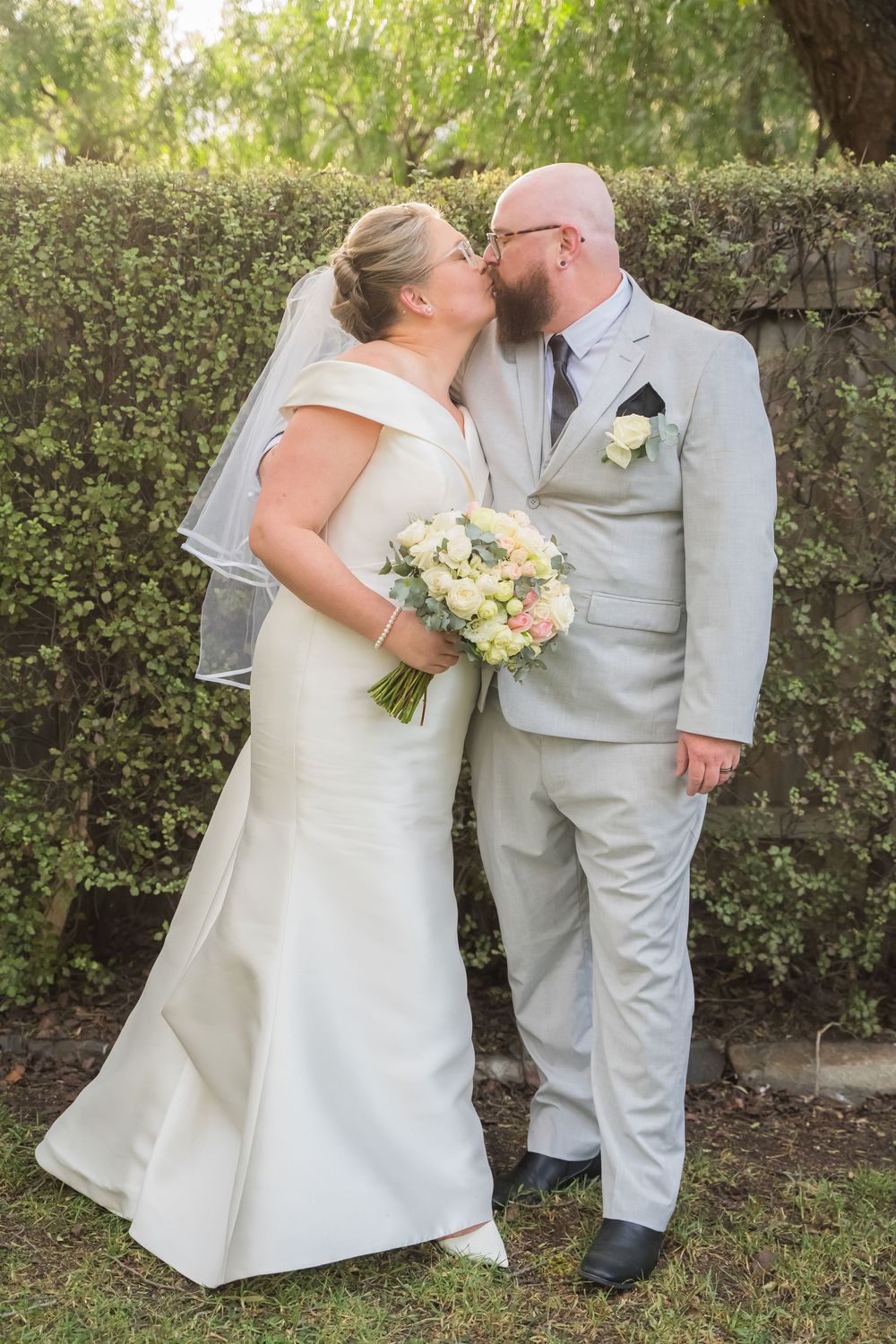 Wedding couple shares intimate moments in a garden setting with white dress and light gray suit.