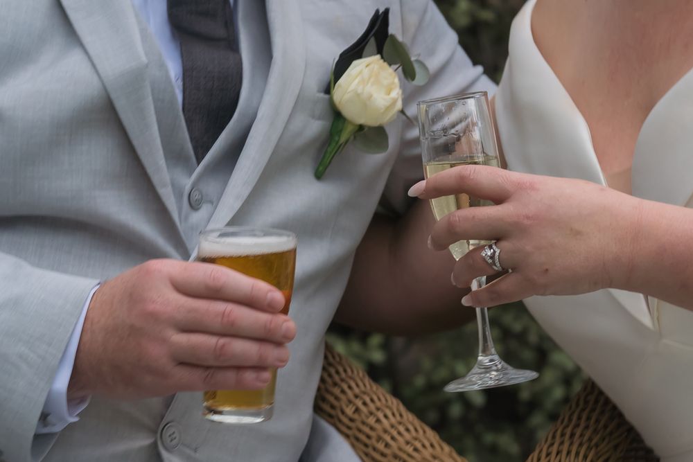 Wedding party members holding drinks and toasting with champagne and beer glasses at an outdoor reception.
