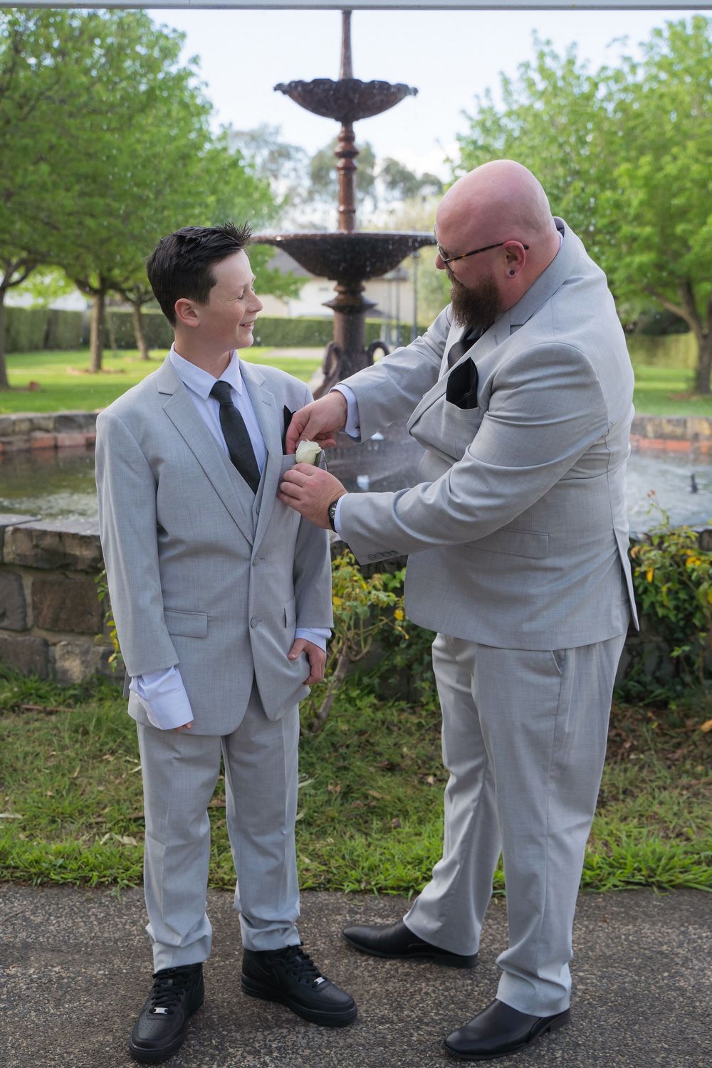A series of photos showing a sweet moment between an adult and child in matching light gray suits outdoors by a fountain.