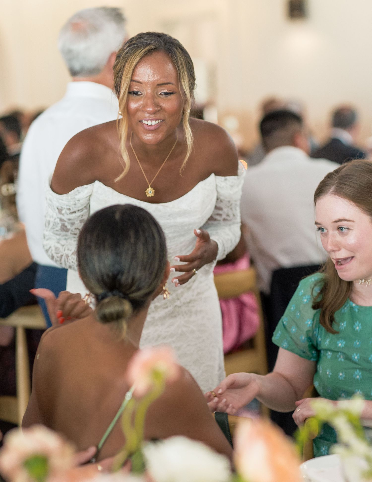 Wedding guests share joyful laughter during an indoor celebration with natural lighting and floral decorations.