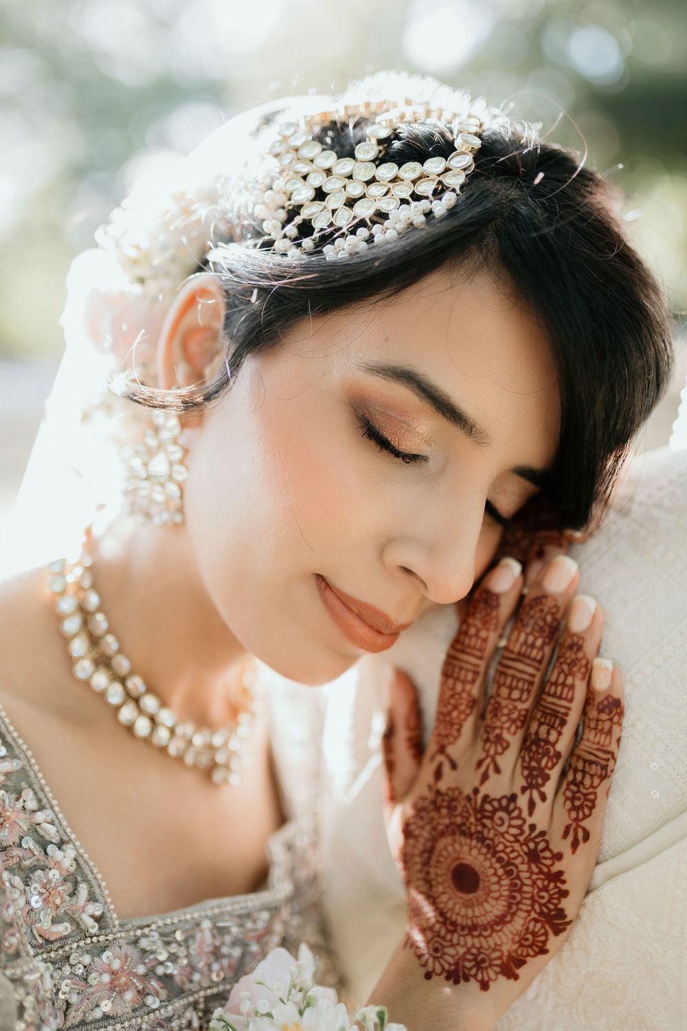 Artistic close-up portrait of a bride showing intricate henna design on her hand with pearl jewelry details.
