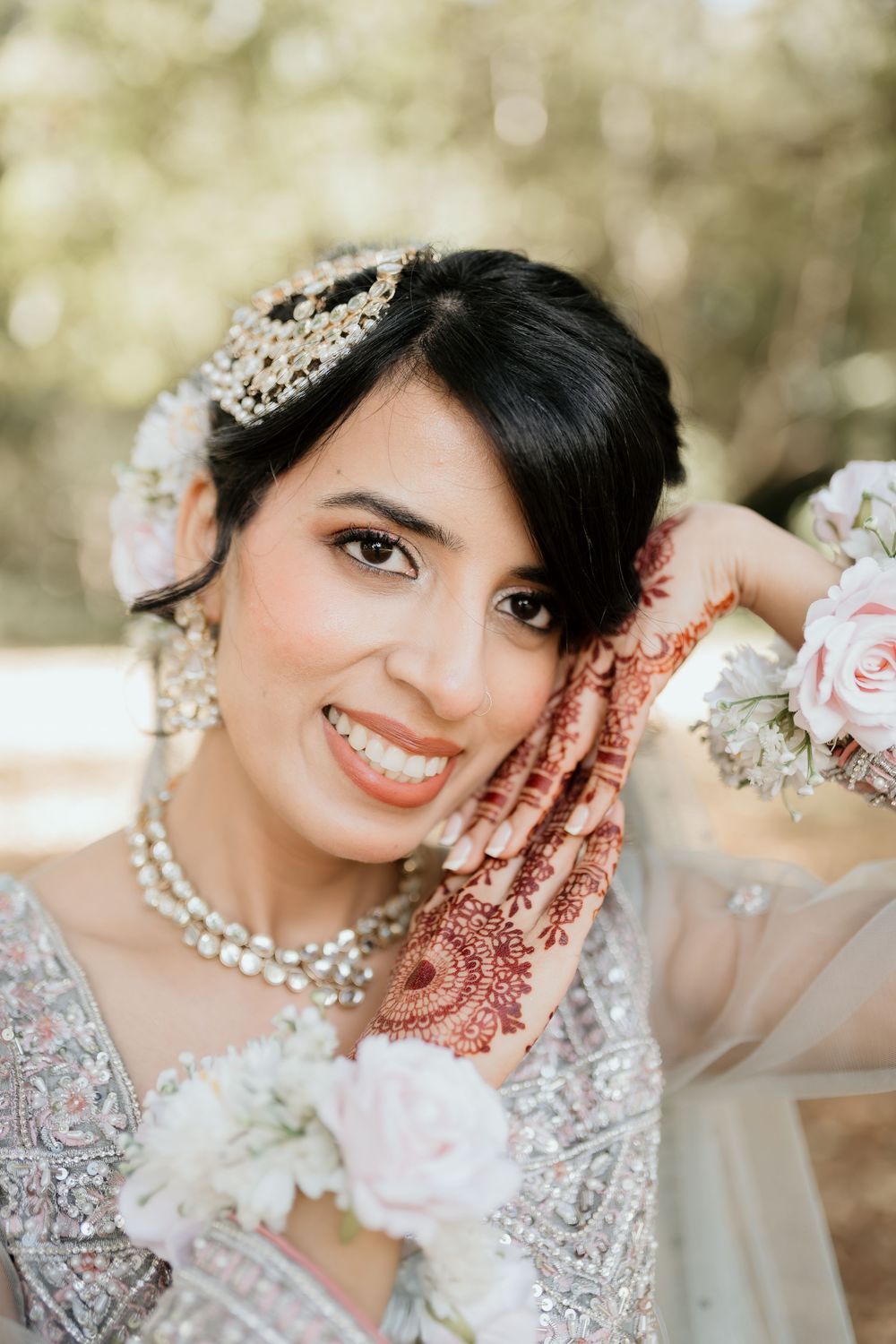 A close-up portrait of someone wearing traditional Indian bridal attire with henna designs and intricate jewelry details.