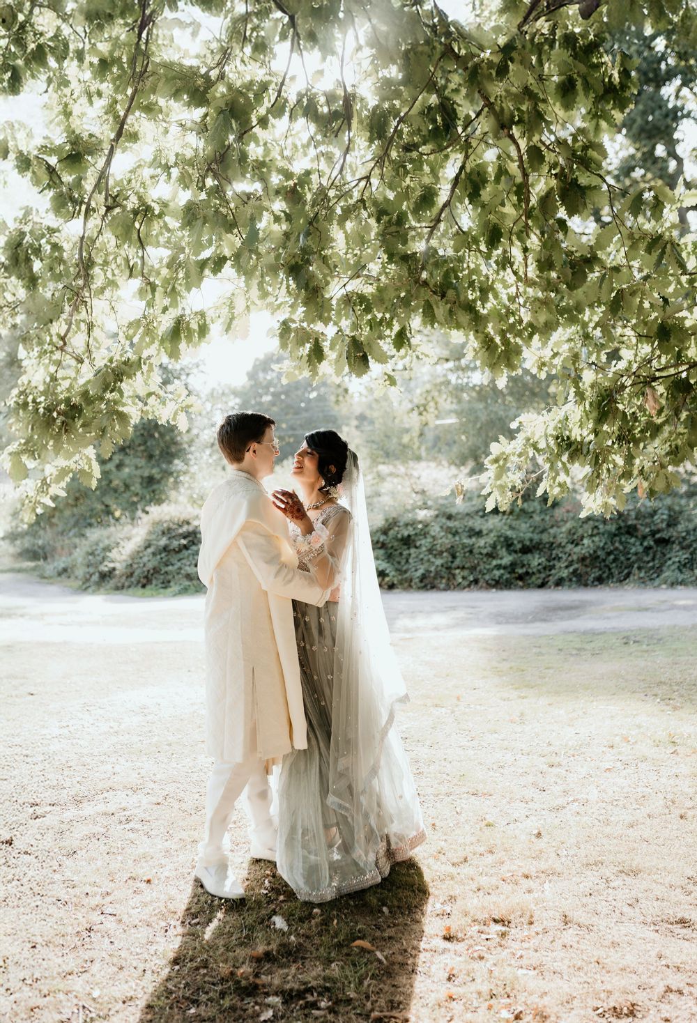 Romantic wedding couple shares intimate moments under a tree canopy in soft natural lighting.