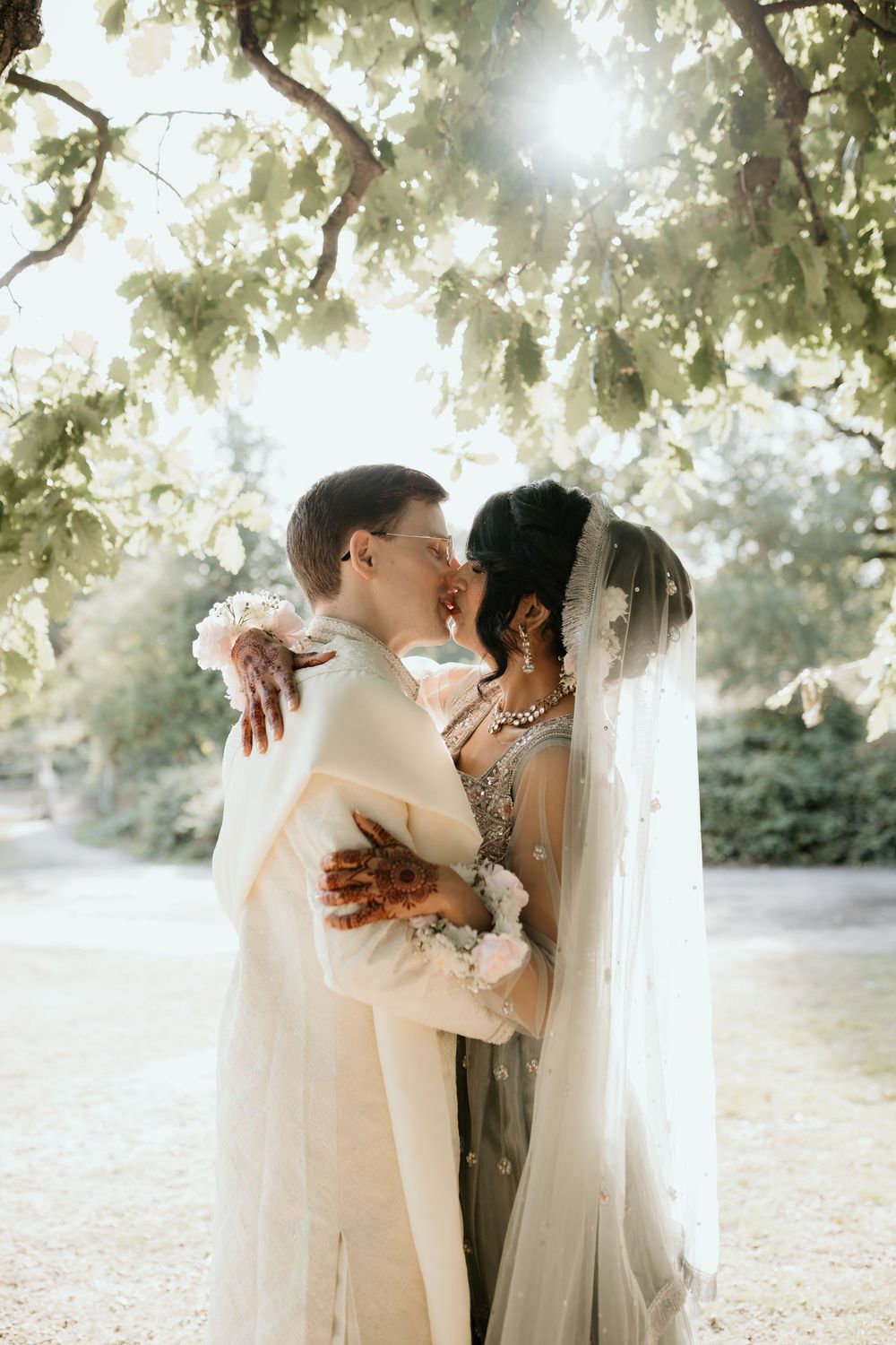 Romantic wedding couple shares intimate moments together under sunlit trees in an outdoor garden setting.