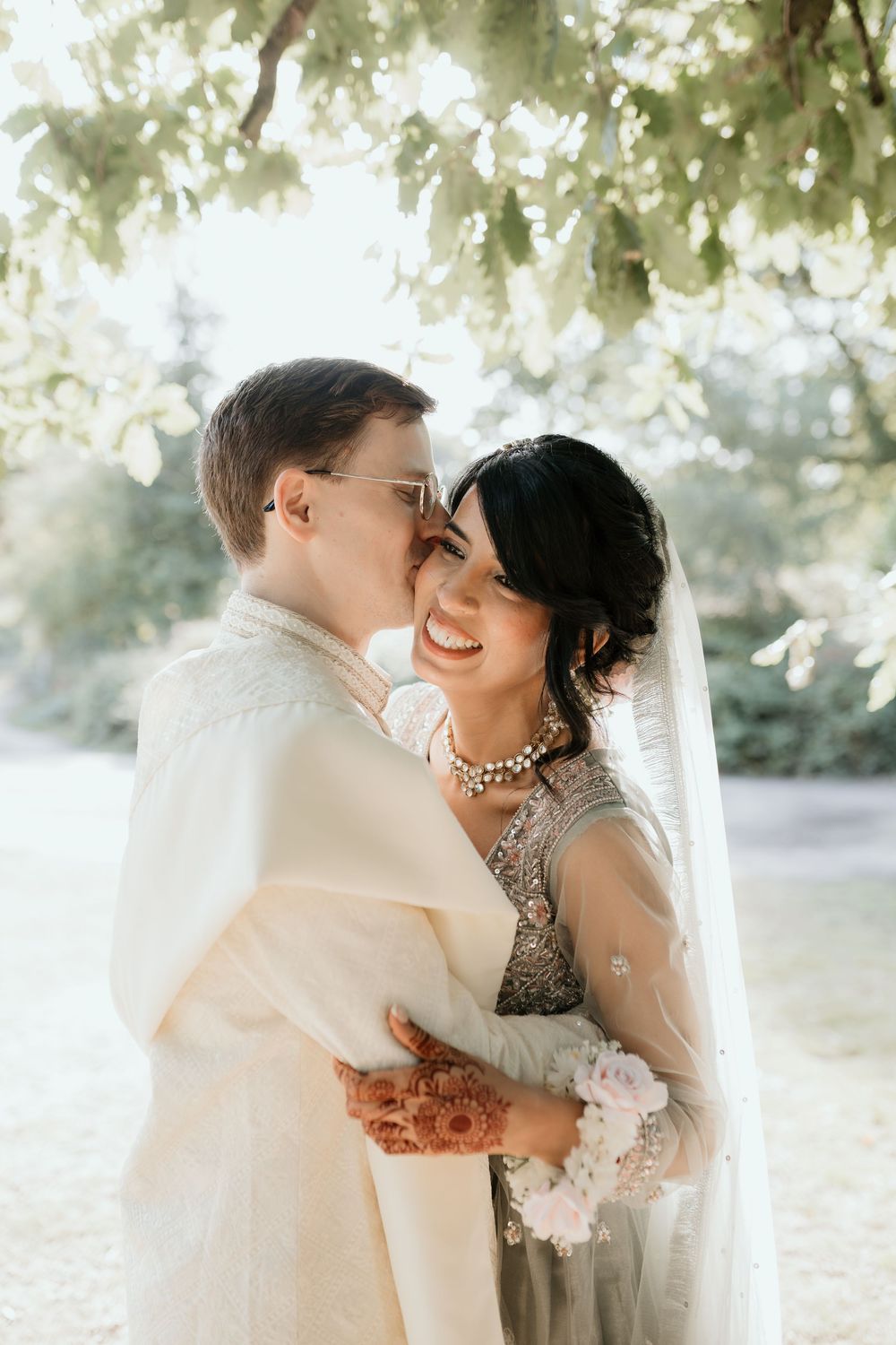 Newlyweds share loving moments in dreamy garden setting with filtered sunlight.