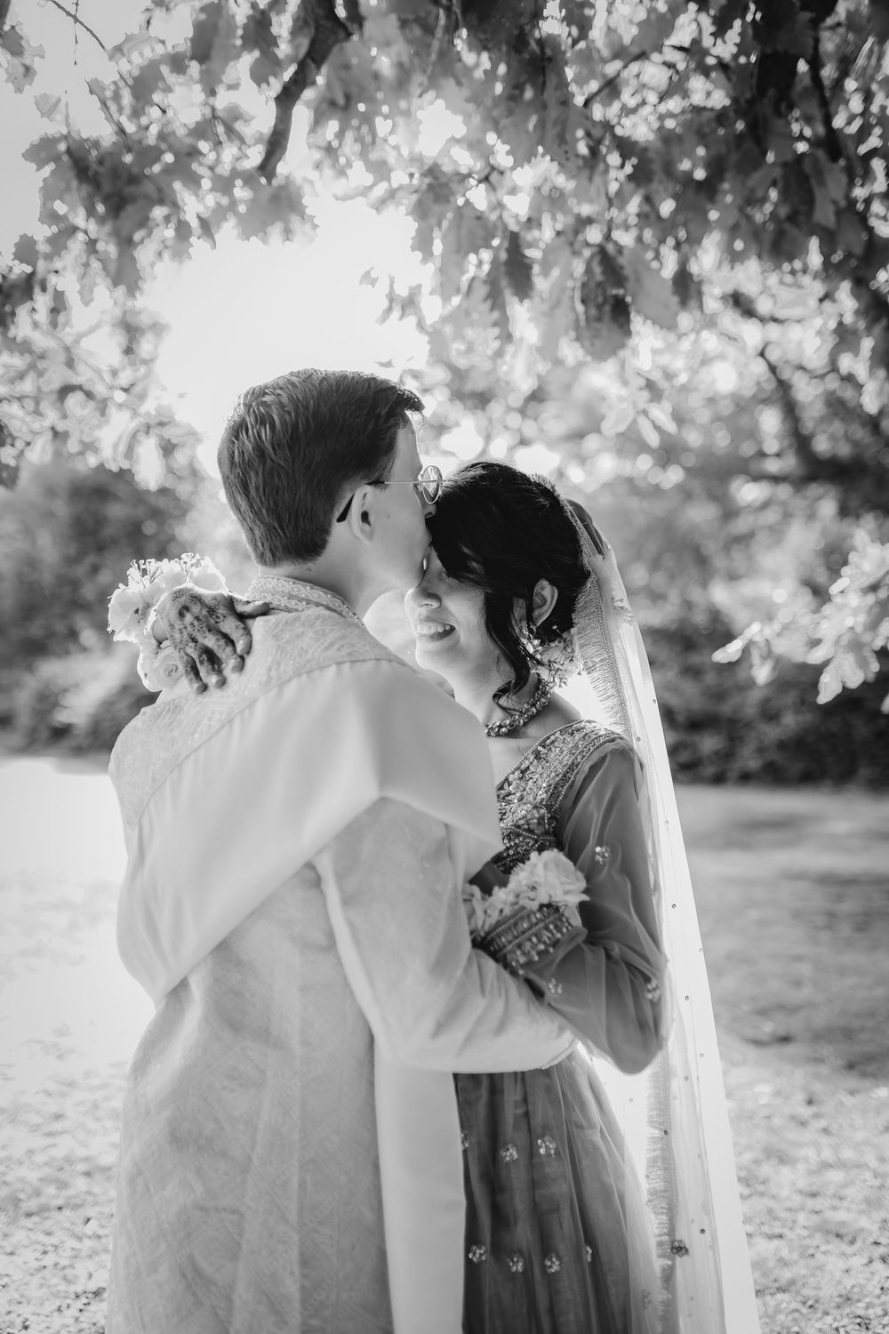 Black and white wedding photography captures intimate moments between couple under trees.