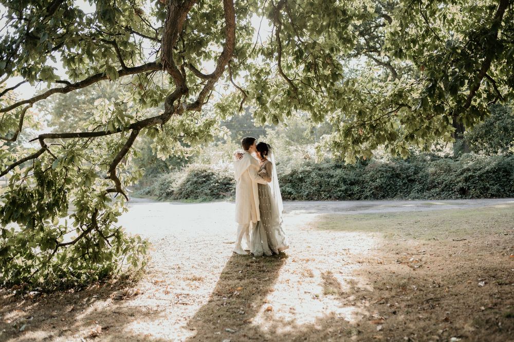 A beautiful sun-filled forest wedding ceremony setup with white chairs and natural greenery overhead.