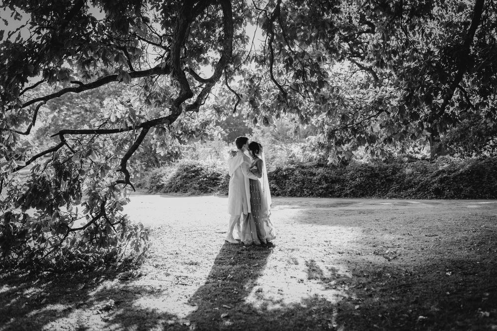 Black and white outdoor wedding scene with trees casting dramatic shadows across a grassy landscape.