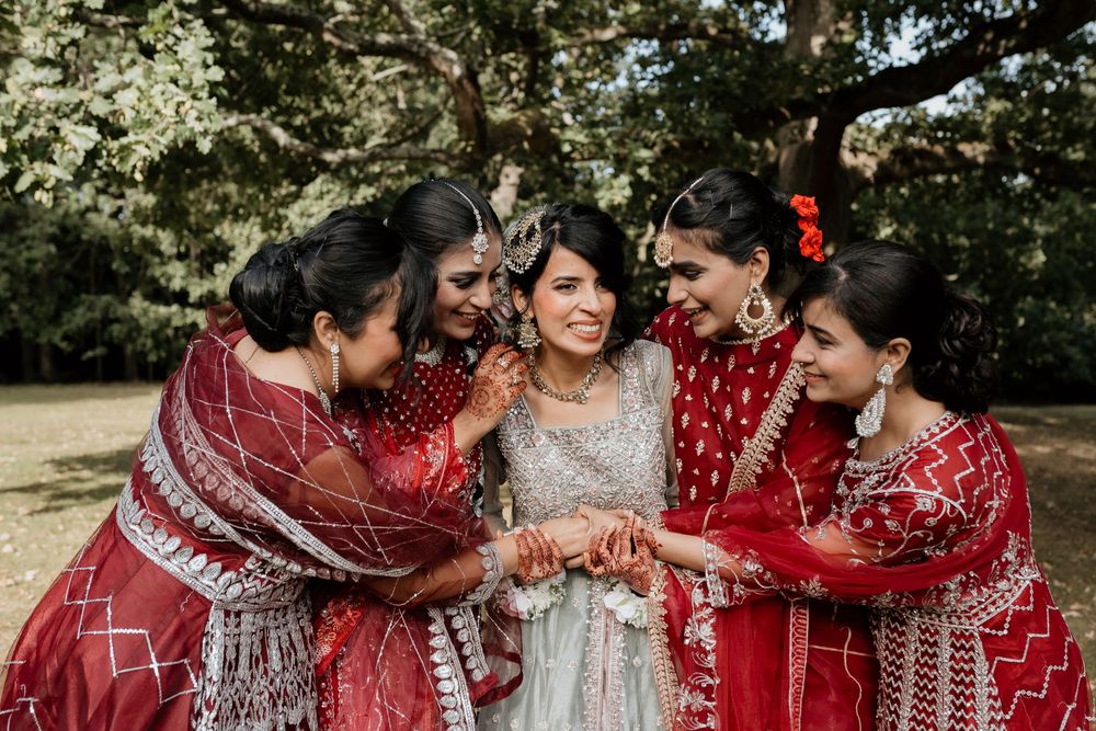 Bridesmaids in matching red and silver sequined sarees hold hands at a traditional Indian wedding ceremony.