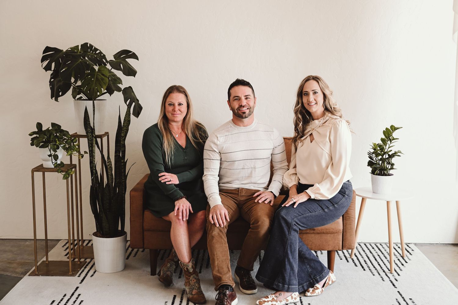 Group sitting casually on white floor with indoor plants and modern minimalist decor.