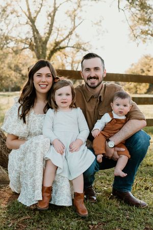 A family of four sits together outdoors on a fall day.