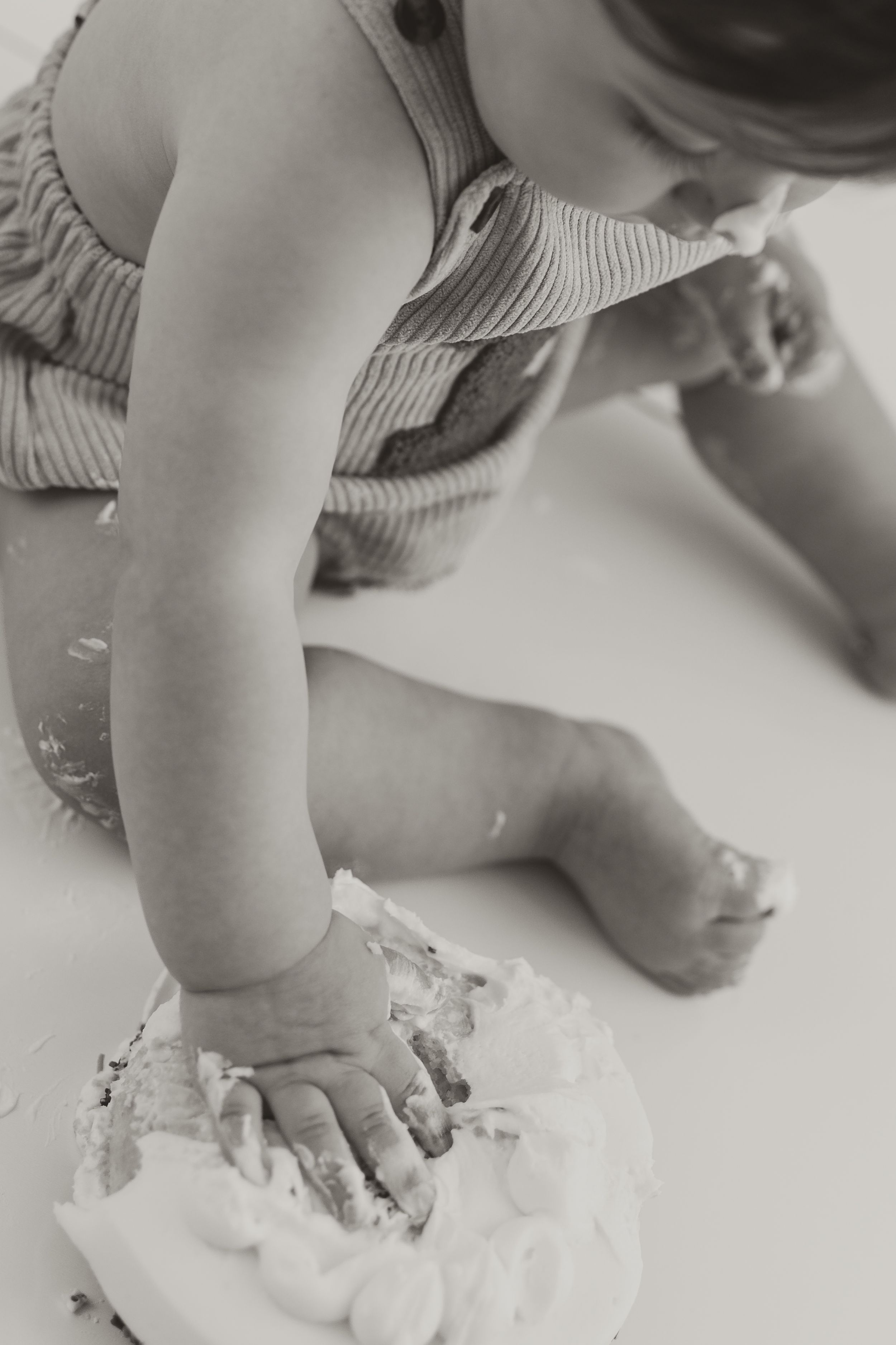 Black and white photo of a baby smashing cake with hands during first birthday cake smash photoshoot.