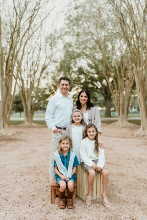 A family poses together on wooden crates along a tree-lined path.