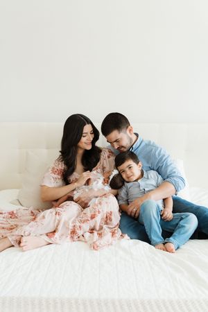 A family relaxes together on a white bed with their newborn baby.