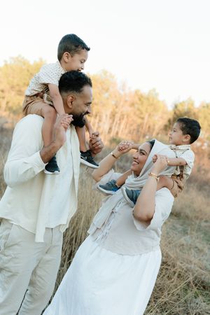 Happy family with two young children on their shoulders playing in a golden field during sunset.