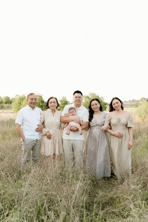 A multigenerational family poses together in a field wearing neutral colored clothing.