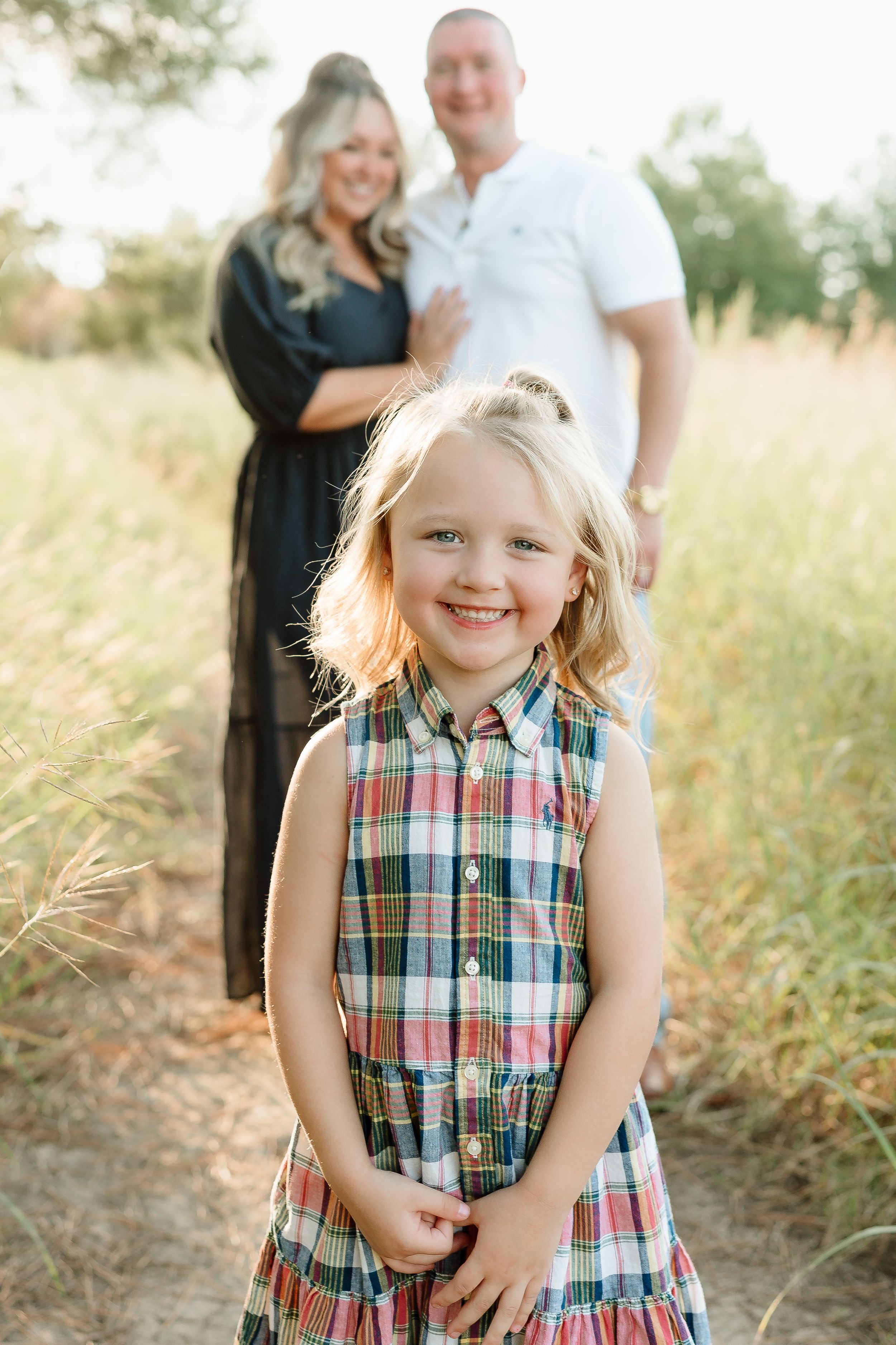 Joyful outdoor family photo session in golden grass field at sunset.