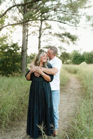 Romantic couple embraces on tree-lined path during outdoor photo session.