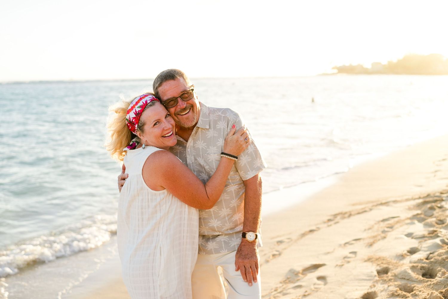 A couple embraces joyfully on a sun-drenched beach during golden hour photography session. Oahu family photographer