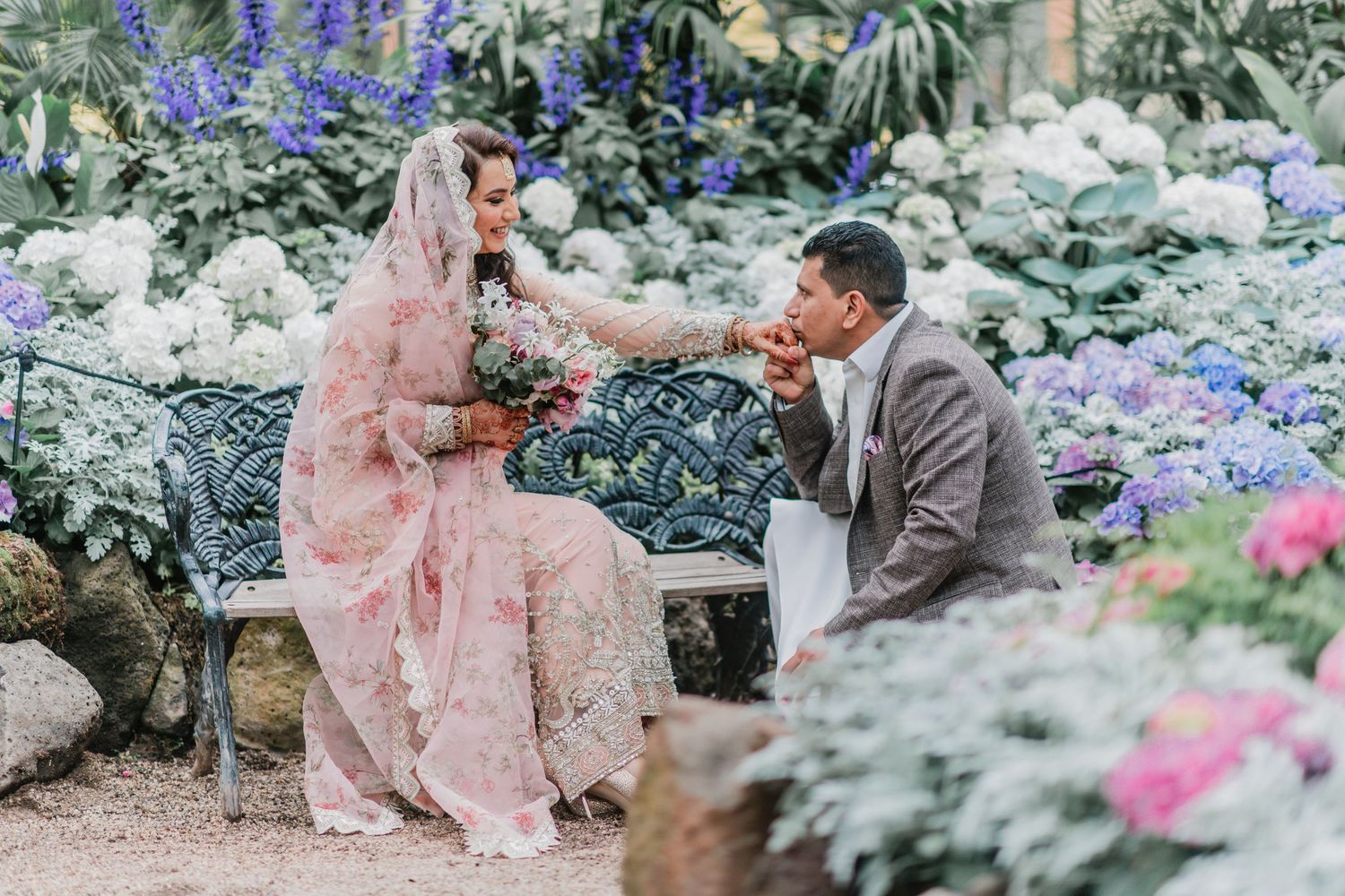 A romantic couple shares tender moments in a lush garden setting filled with blooming blue and white flowers.