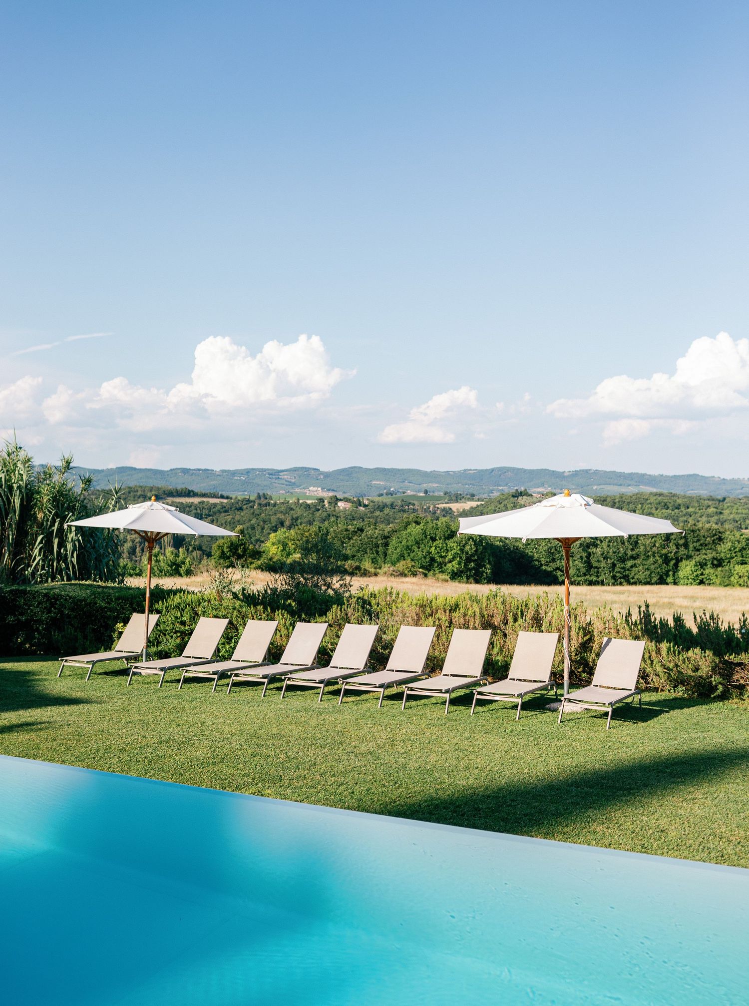 Scenic infinity pool with lounge chairs and umbrellas overlooking rolling green hills in the Italian countryside at Borgo Stomennano.