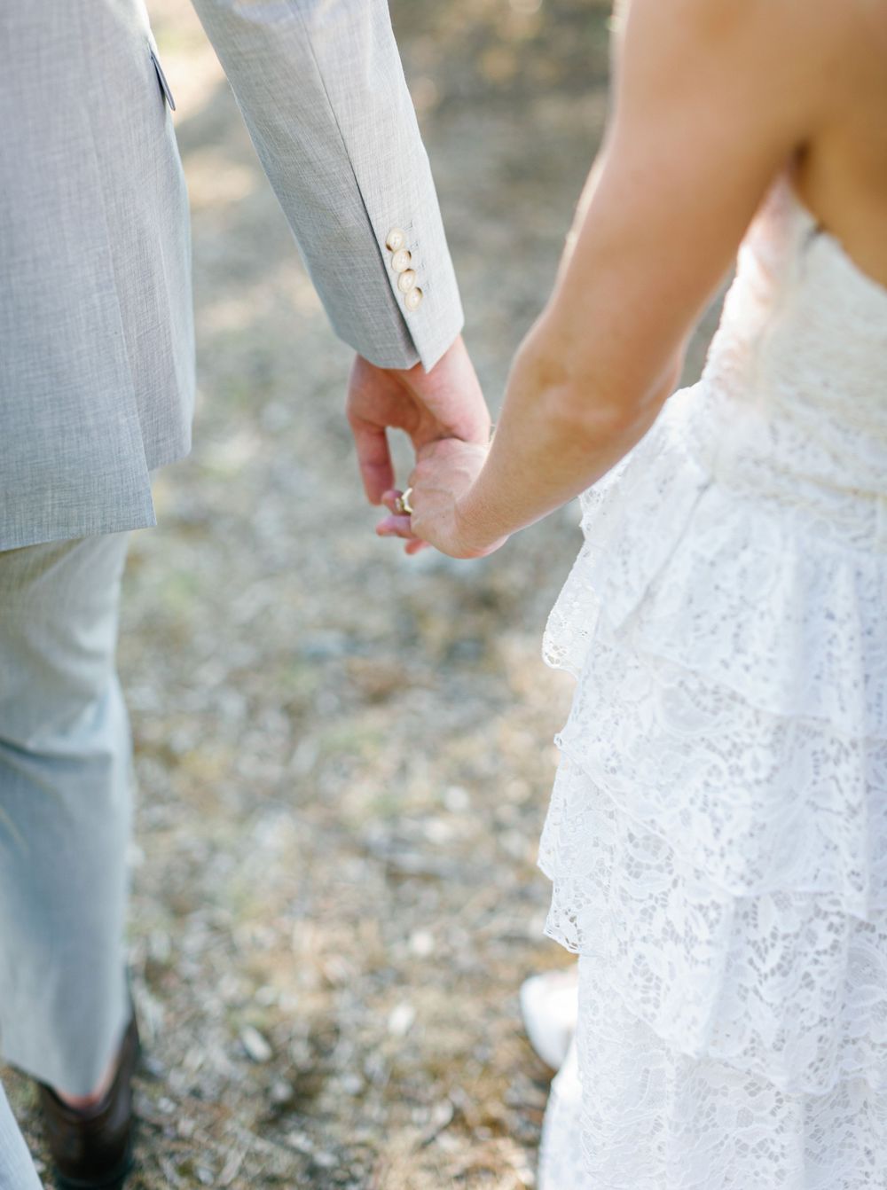 Close up sequence shows couple joining hands and arms while wearing gray suit and white lace wedding attire.