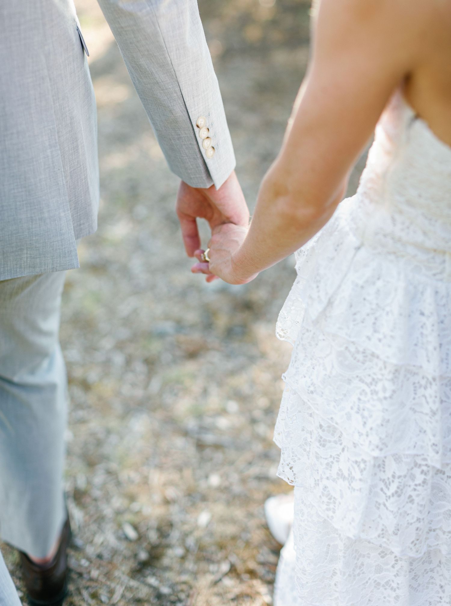 Close up sequence shows couple joining hands and arms while wearing gray suit and white lace wedding attire.