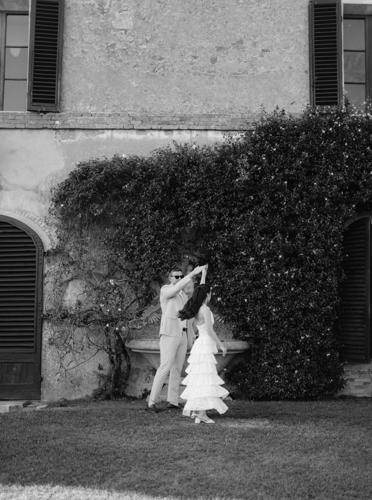 A graceful sequence of black and white photographs showing two figures dancing beside a hedge in a courtyard.