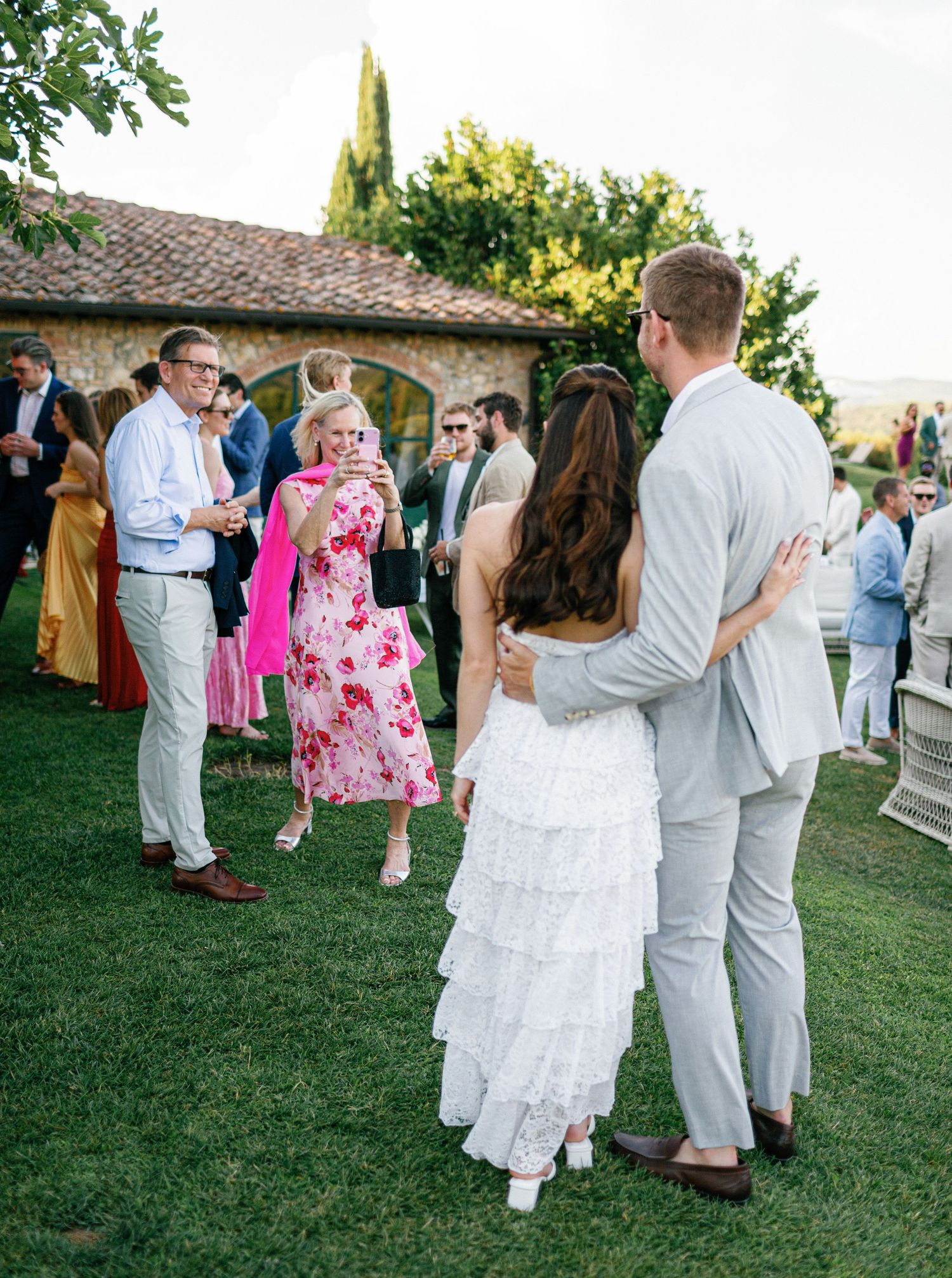 Party guests dance and mingle on a green lawn at an outdoor celebration during the golden hour.