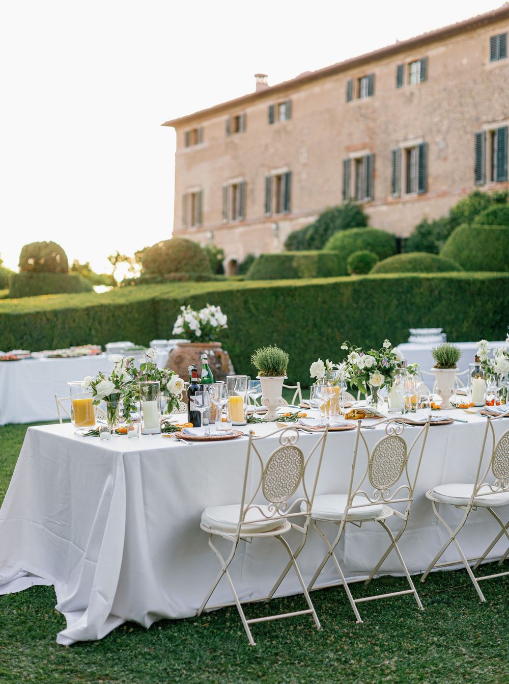 Elegant outdoor wedding reception tables set at Borgo Stomennano with white linens and gold chairs along a manicured garden path at sunset.