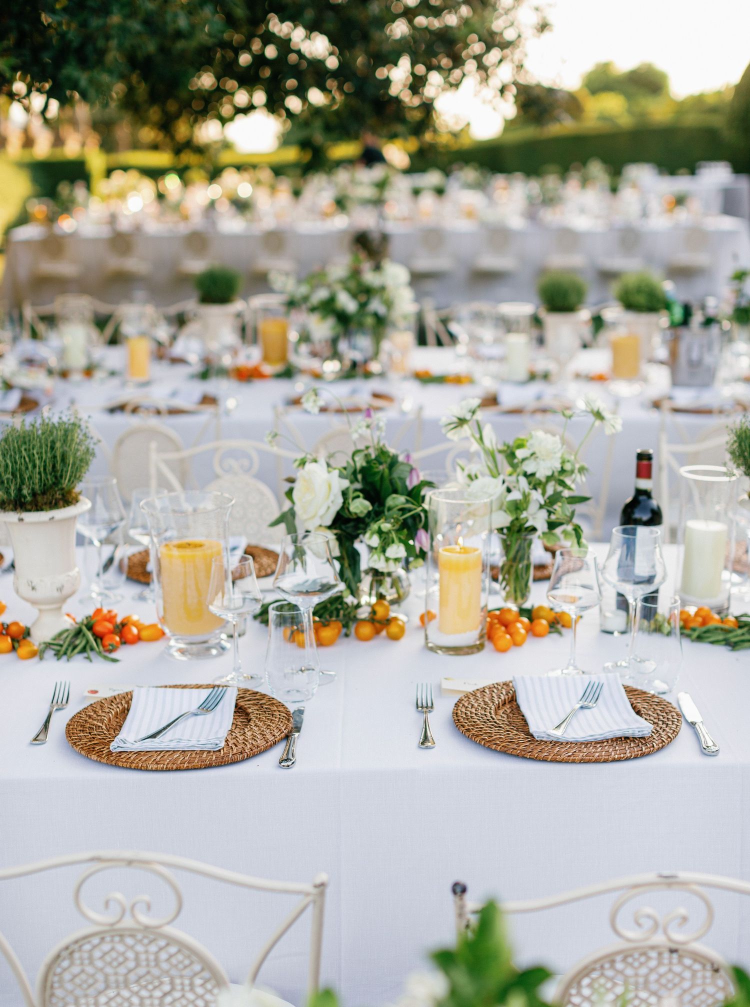 Elegant outdoor wedding reception tables set with white linens, wicker placemats, and fresh greenery decorations.