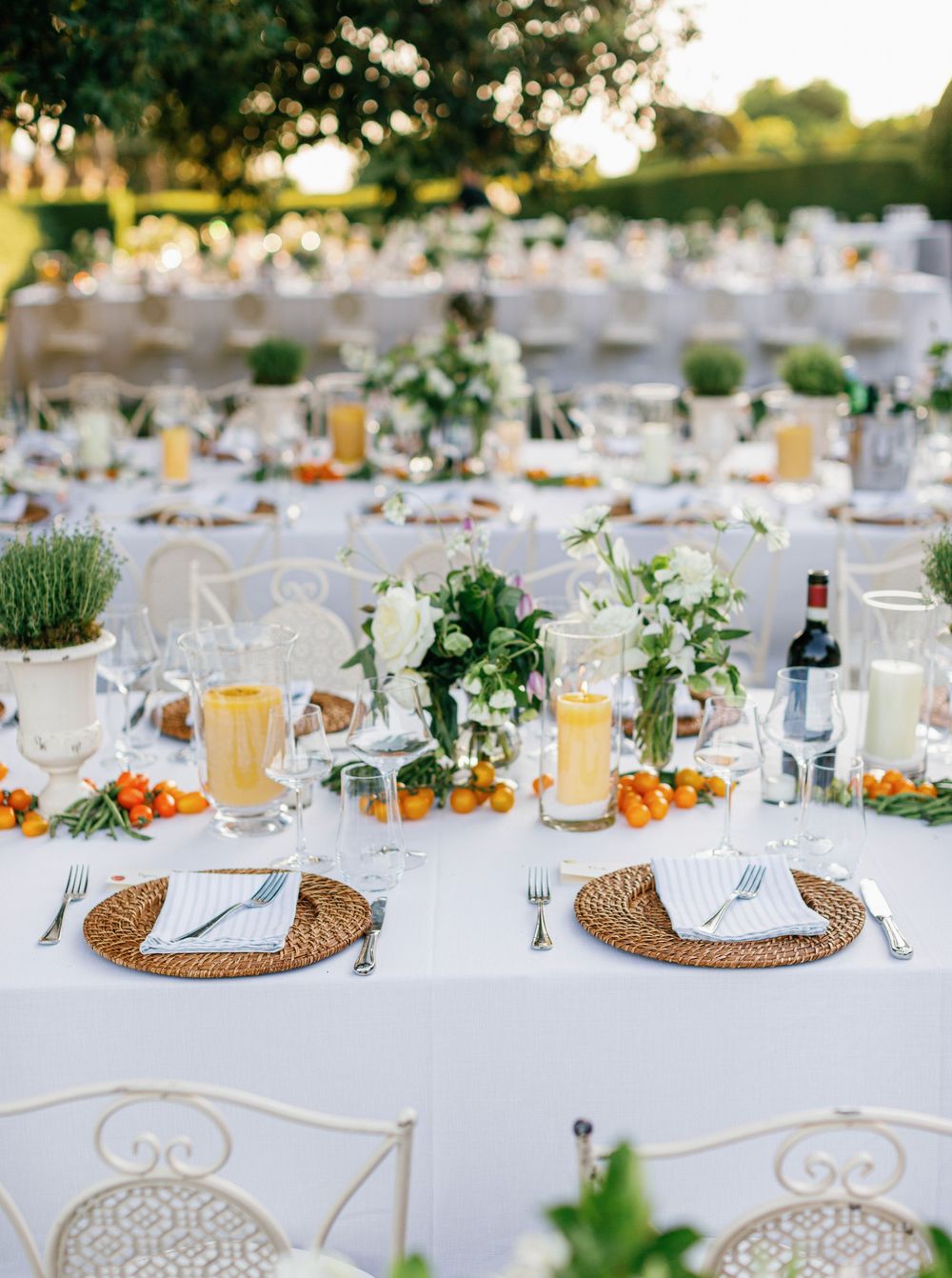 Elegant outdoor wedding reception tables set with white linens, wicker placemats, and fresh greenery decorations.