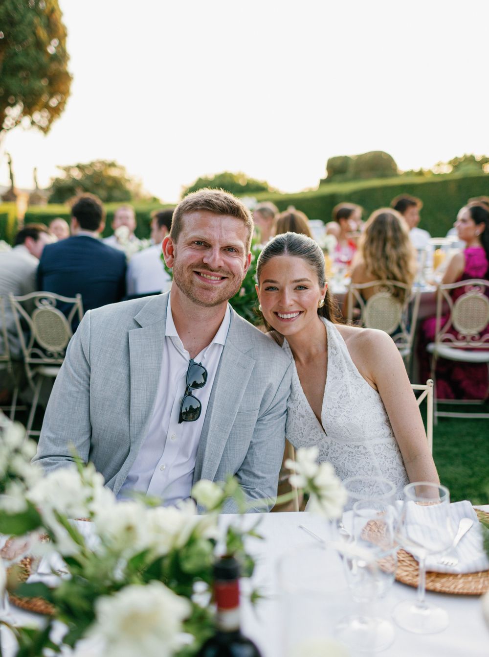 Wedding couple at an outdoor reception smiling together at table with white floral centerpieces.