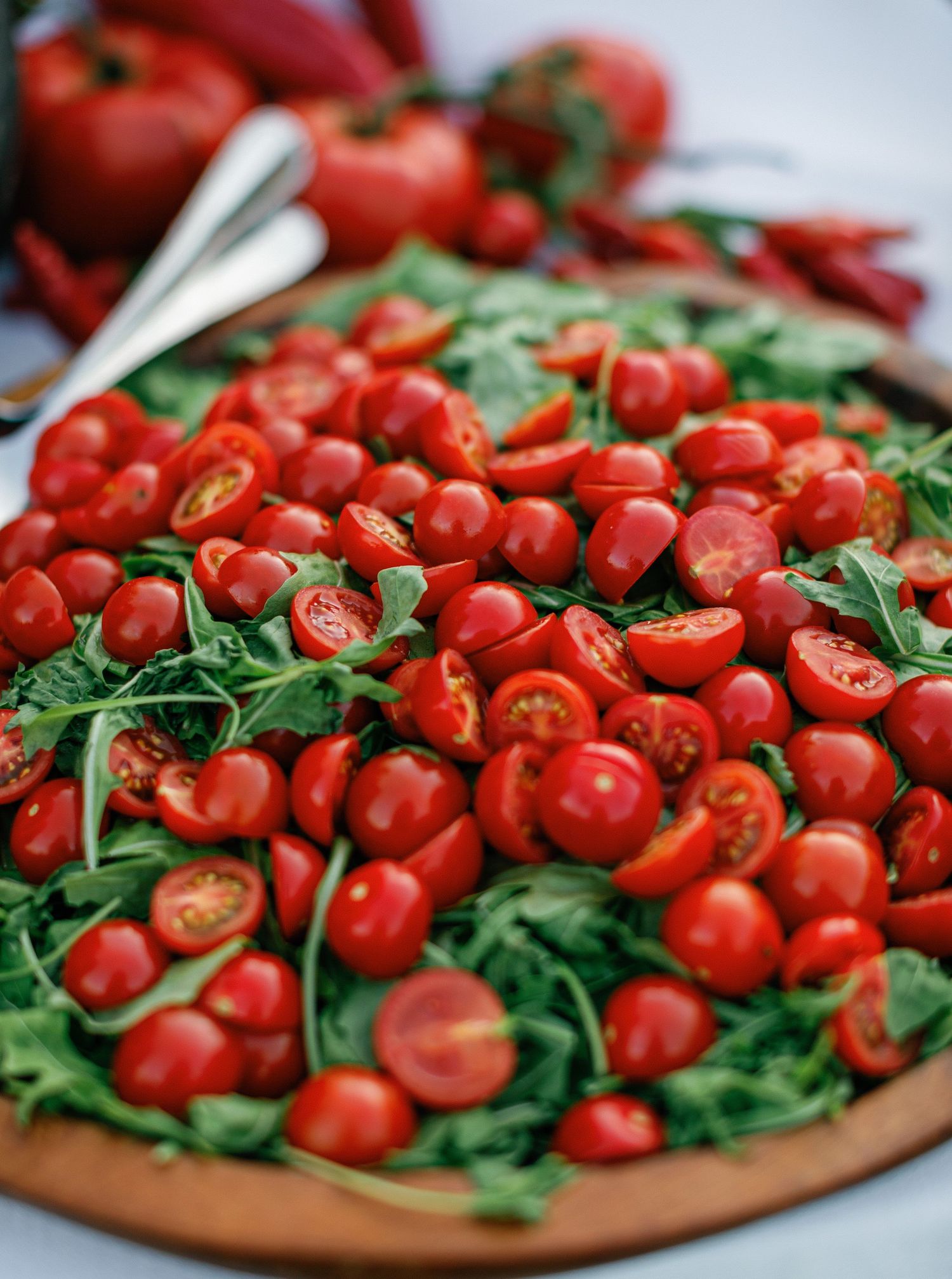 Fresh halved cherry tomatoes and baby arugula displayed on a rustic wooden cutting board in natural light.