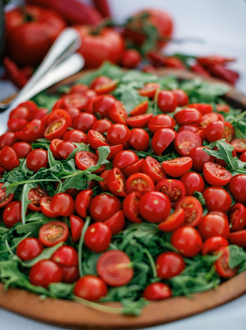 Fresh halved cherry tomatoes and baby arugula displayed on a rustic wooden cutting board in natural light.