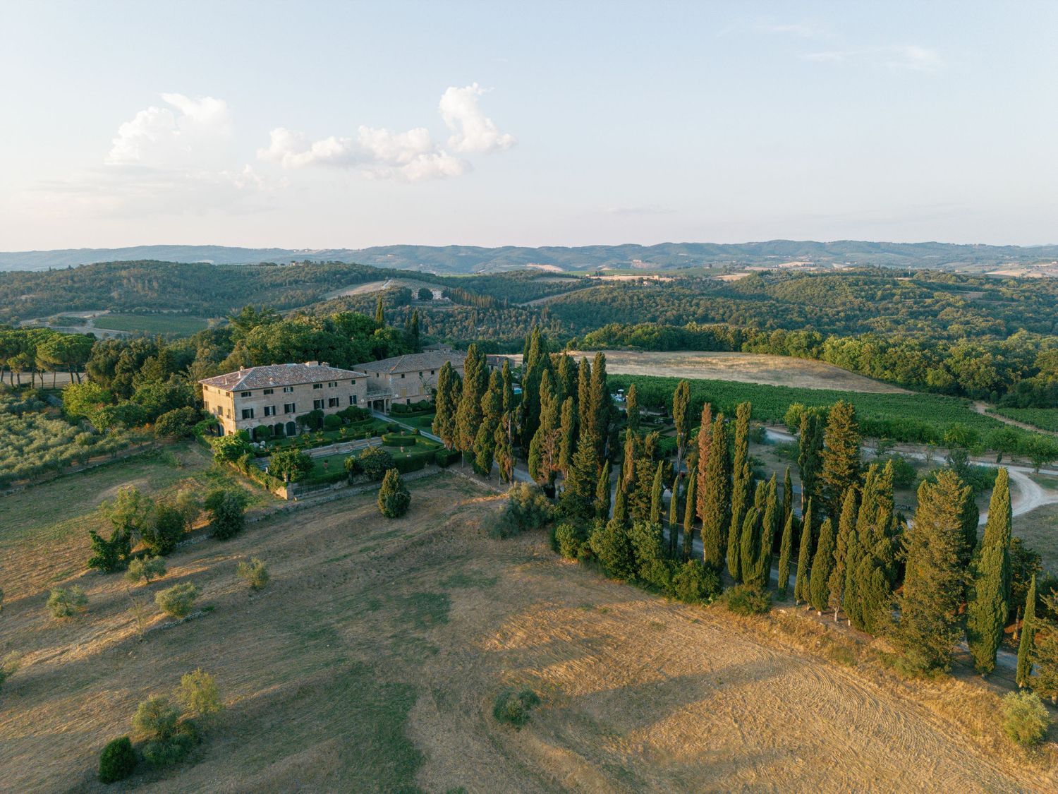 Panoramic view of rolling Tuscan hills and Borgo Stomennano with cypress trees dotting the verdant countryside landscape in Italy.