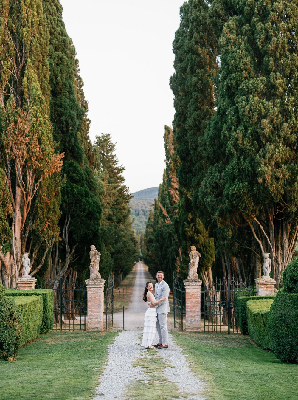 Couple walking and embracing along a scenic cypress tree-lined path at Borgo Stomennano in Tuscany at sunset.