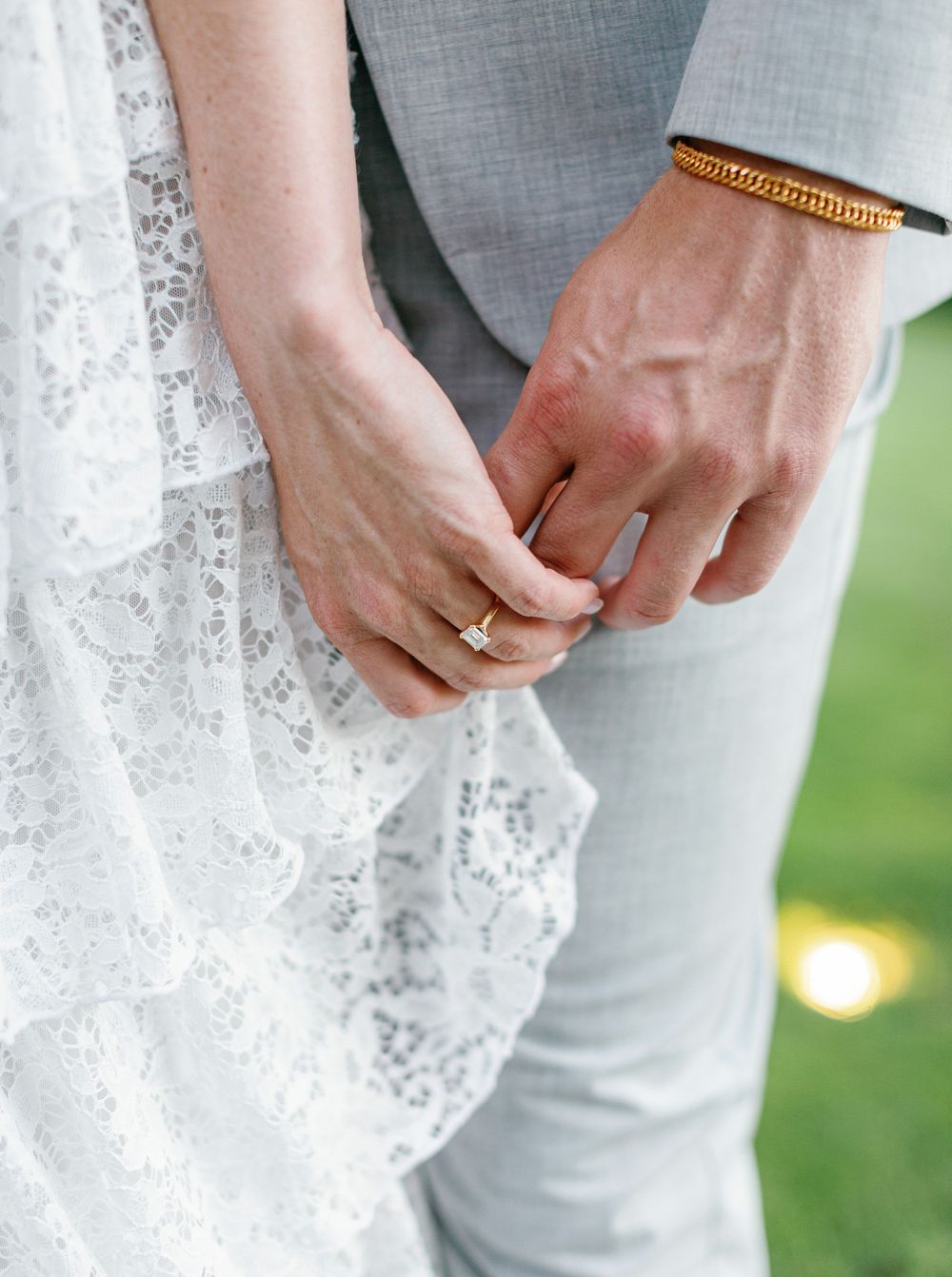 Close-up detail shots of lace wedding dress fabric and rings being held by hands against an outdoor background.