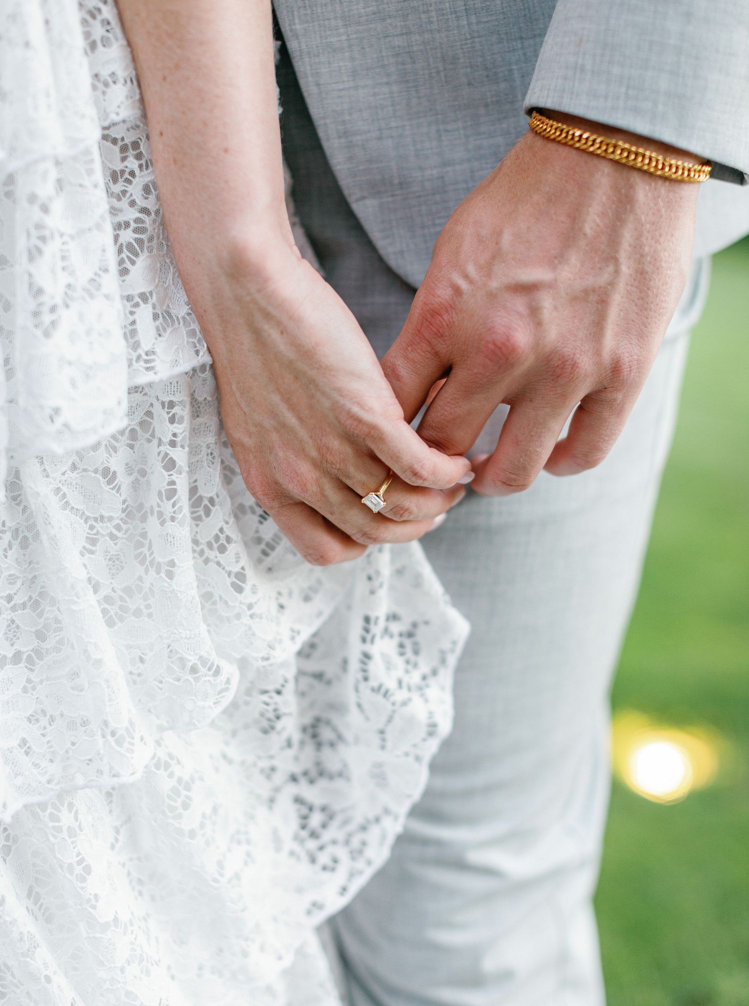 Close-up detail shots of lace wedding dress fabric and rings being held by hands against an outdoor background.