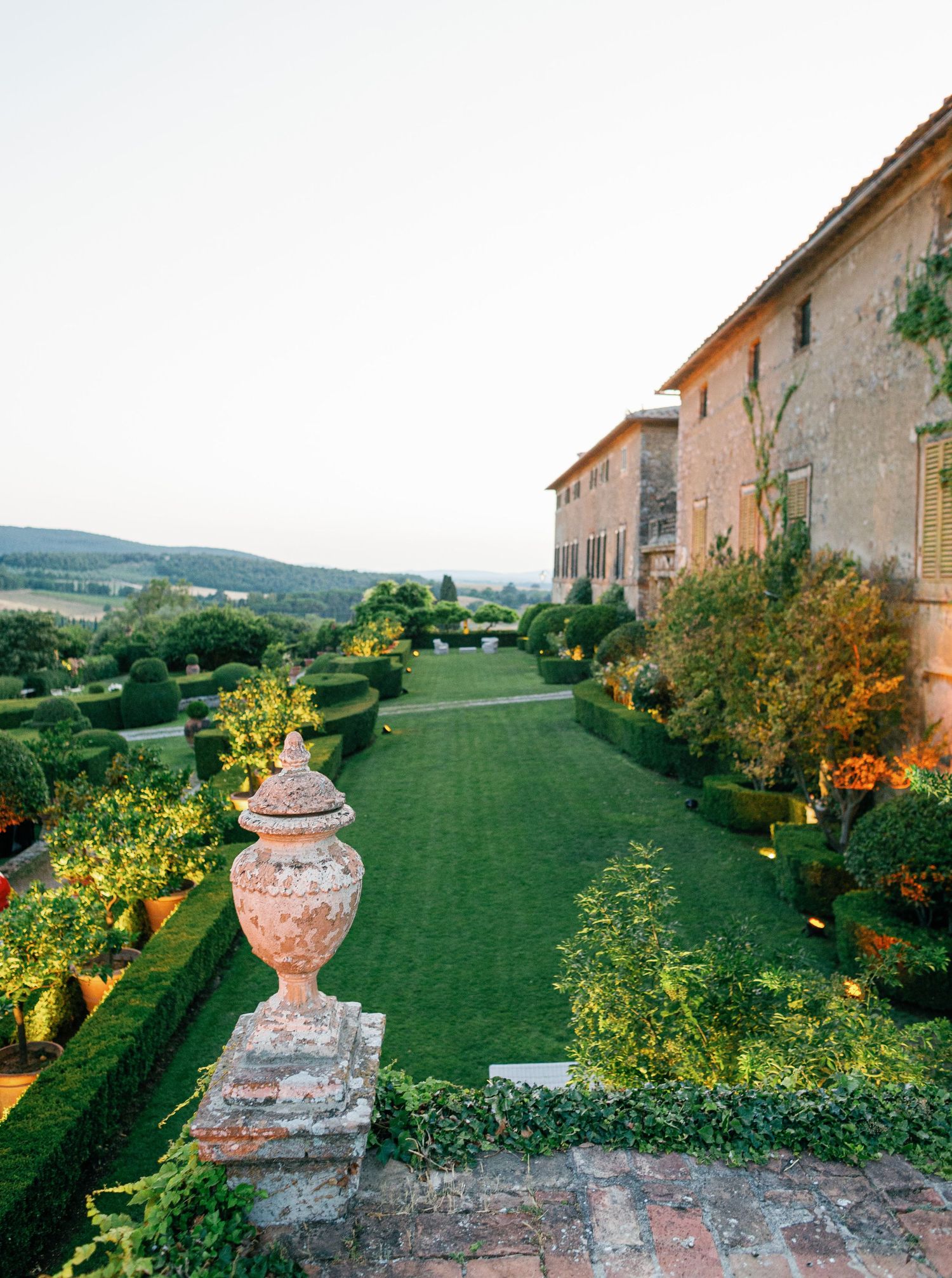 Scenic garden terrace at Borgo Stomennano in Tuscany with stone balustrades and manicured lawns overlooking rolling countryside at sunset.