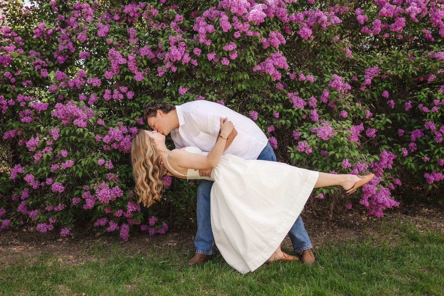 A romantic photo series shows a couple in wedding attire posing together against a backdrop of vibrant lilac bushes. utah family photo