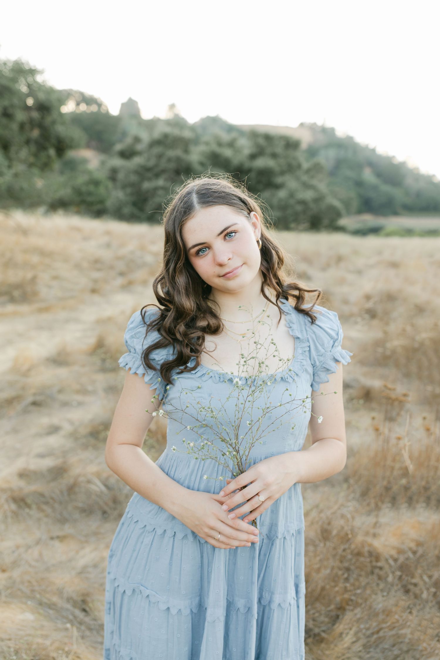 A tender embrace is shared in a soft sage grey dress outdoors at sunset near a serene pond captured by Chelsee Rawe Photography.