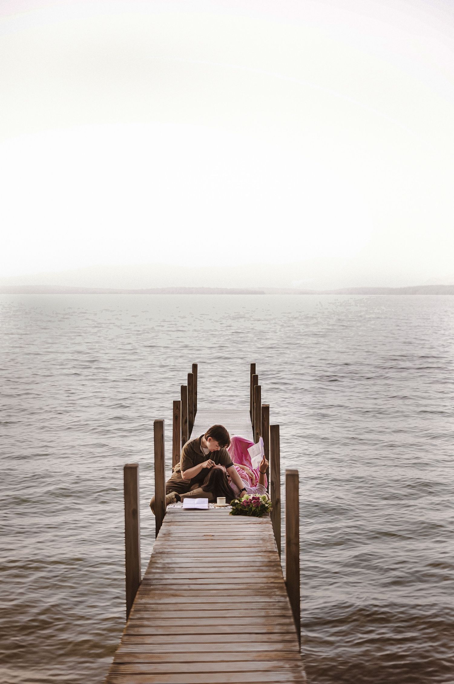 Couple sitting intimately at the end of a wooden pier surrounded by calm open water.