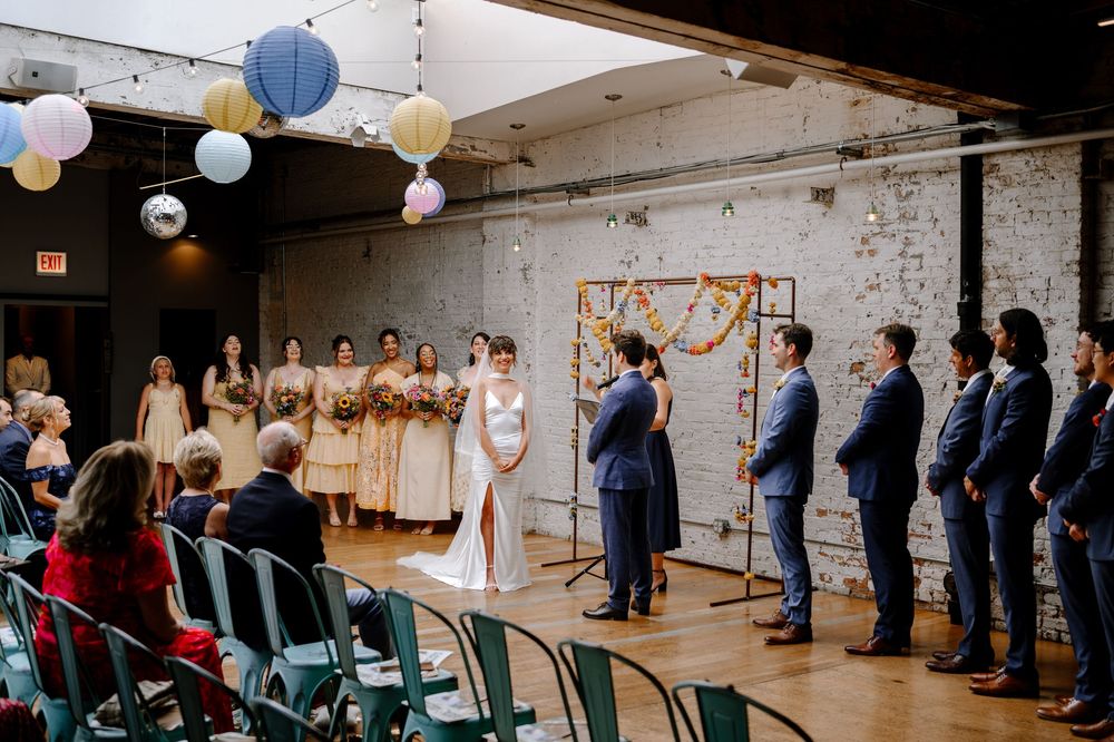 Wedding ceremony in an industrial loft space with exposed brick walls and hanging balloon decor.