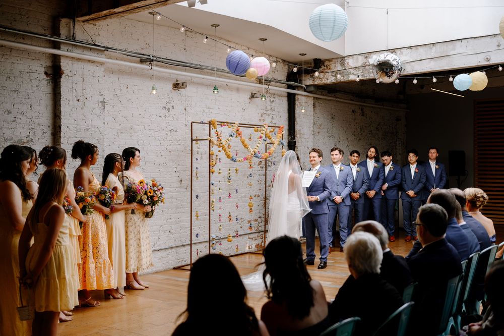 Panoramic view of wedding ceremony in a minimalist industrial space with white paper lantern decorations.