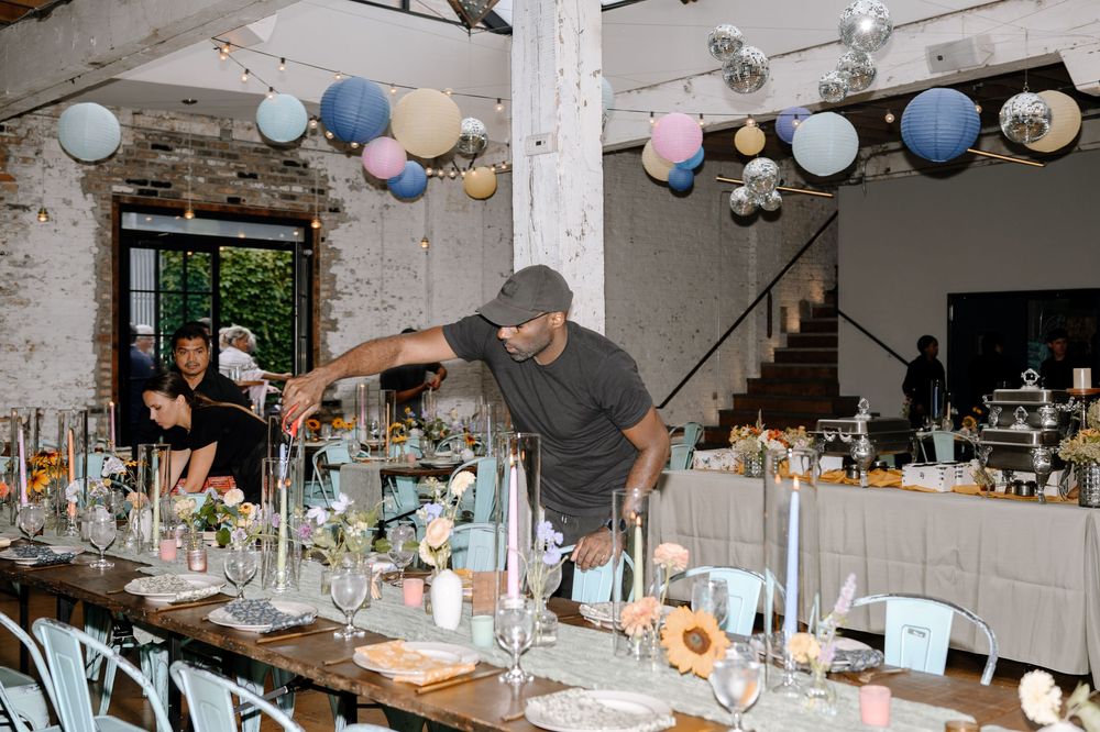 Long wooden tables decorated with candlelight and place settings under festive paper lanterns in a rustic venue.